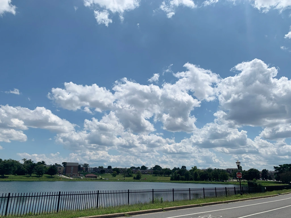 Bright blue sky peppered with fluffy white clouds above a reservoir along a bike path.